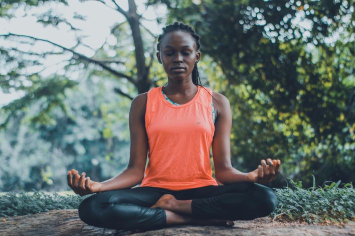 A woman meditating peacefully outdoors in a lush green setting, promoting relaxation and mindfulness.