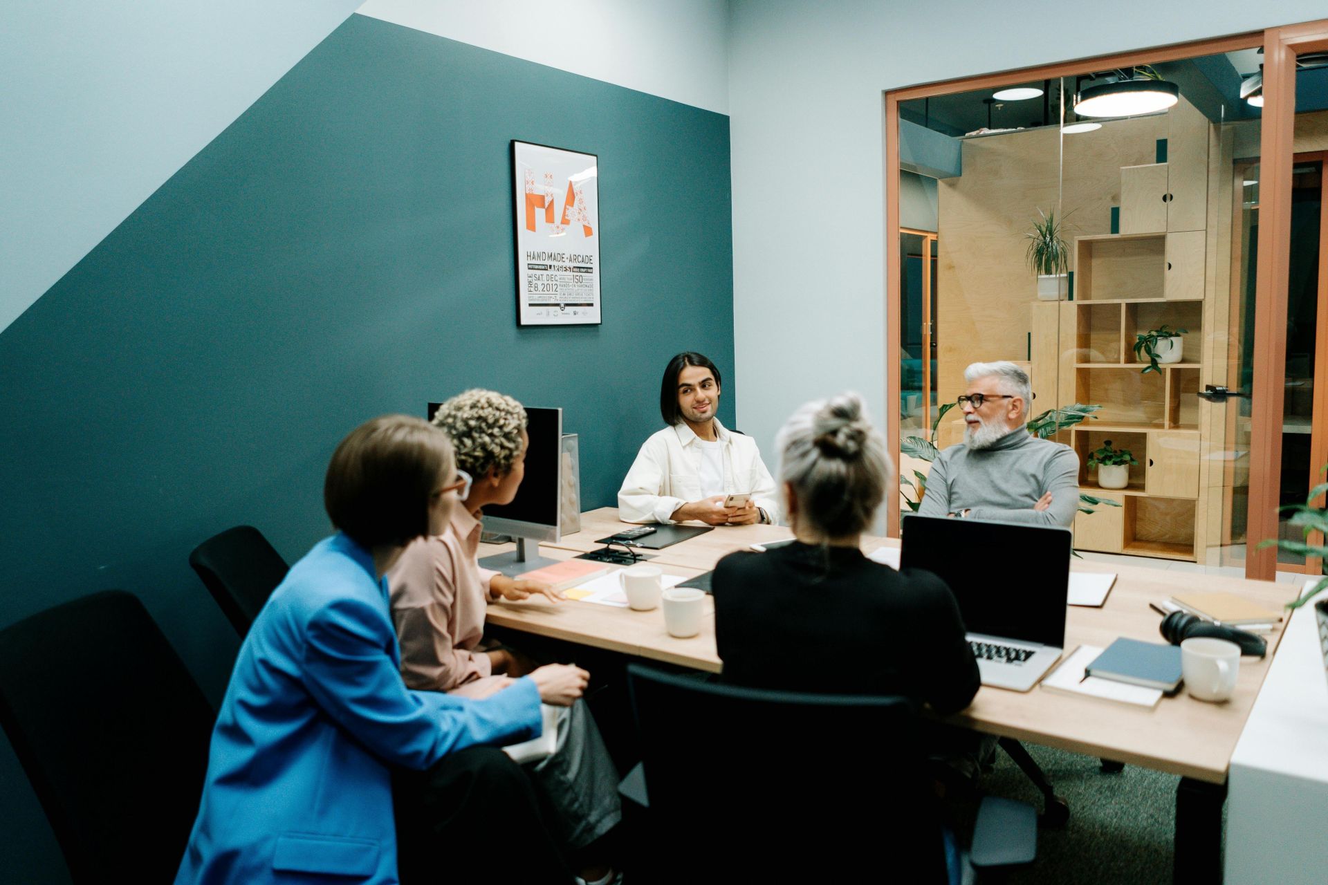 Diverse group of professionals having a meeting in a modern office setting, discussing projects with laptops and notes.